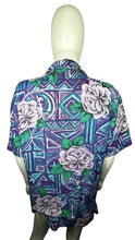 Load image into Gallery viewer, A medium vintage Partners Mervyns short sleeve button up with a purple and blue all-over floral print. The shirt is missing all of the buttons but one and has been well-worn. Measured FlatChest - 36&quot;Sleeve - 9&quot;Length - 28&quot;